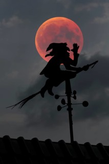 Blood moon over the roof of a house with weather vane with weather witch
