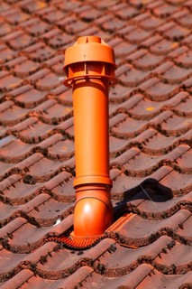 Red chimney made of plastic on a tile roof