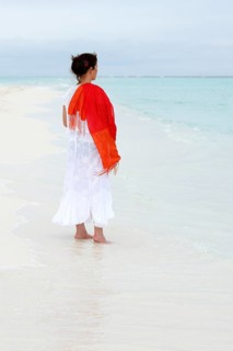 Woman with a red scarf standing on a white beach looking at the turquoise blue sea