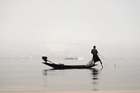 Local fisherman leg rower with wooden boat in the morning fog