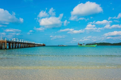 Pier on beach with boats in turquoise water at Saracen Bay on Koh Rong Sanloem island
