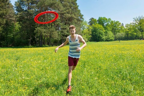 Young man chasing frisbee in meadow