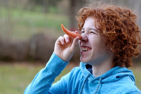 Teenager using a carrot as a long nose