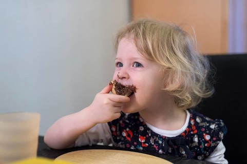 Little blonde girl biting into a bun with chocolate spread