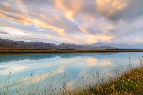Mountains of the Southern Alps reflected in Tekapo Canal with cloudy sky