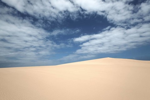 Sand dunes under blue sky with clouds