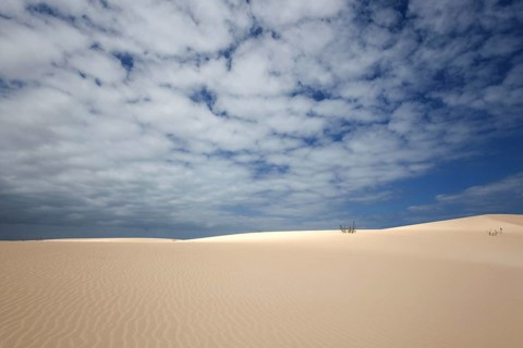 Sand dunes under blue sky with clouds