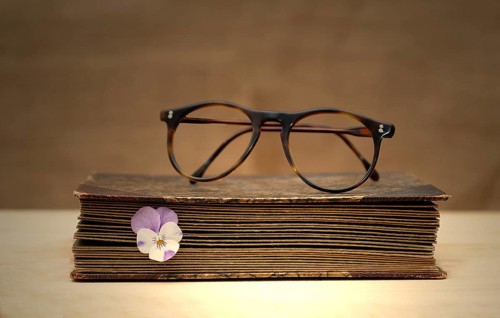Old book with reading glasses and a horned violet