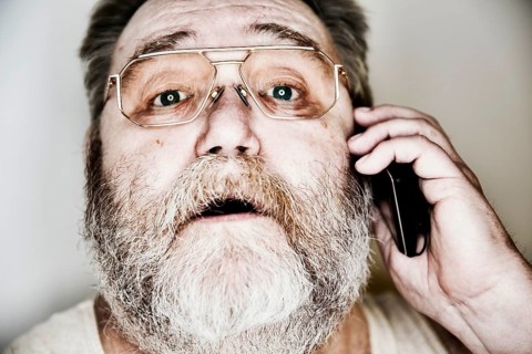 Senior with a full beard and glasses in undershirt on the smartphone