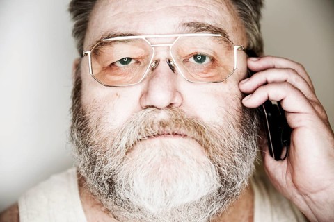 Senior with a full beard and glasses in undershirt on the smartphone