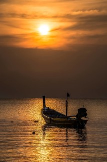 Long-tail boat in sea at sunset