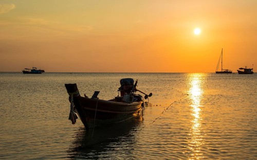 Long-tail boat in sea at sunset