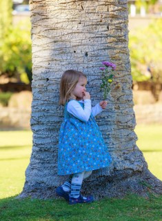 Girl with bouquet leaning against palm trunk