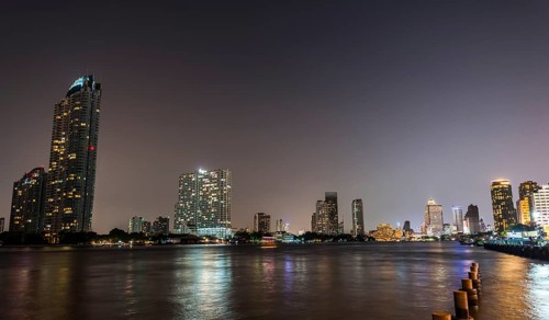 River promenade in the evening with a Ferris wheel and the skyline on the river Mae Nam Chao Phraya