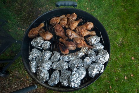 Baked potatoes and chicken legs on grill