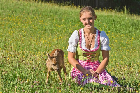 Woman in dirndl with a tame fawn in a flower meadow