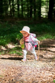 Toddler with doll and walking stick hiking through the woods