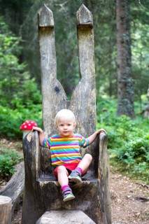 Toddler sitting on a big wooden chair in the forest