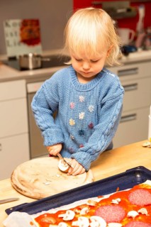 Toddler cutting things and topping a pizza
