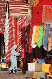 Woman in front of a shop with colourful carpets in the souks of Marrakesh