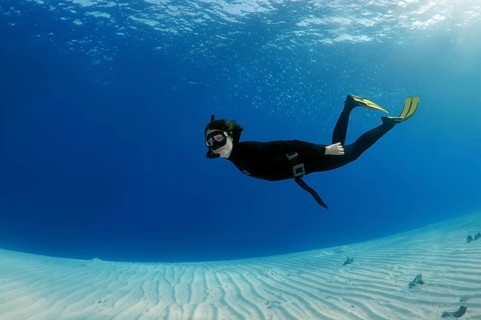 Freediver diving above a sandy bottom