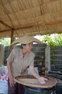 An elderly Thai woman cleans grain rice