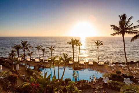 Seaside swimming pool with palm trees at sunset