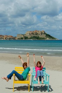 Children sitting in colorful beach chairs on the beach of Calvi