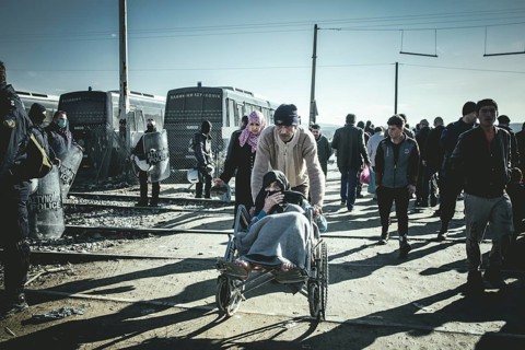 Refugees and old woman in a wheelchair on the border fence