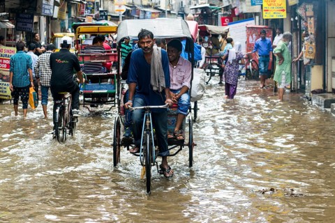 People and cycle rickshaws are moving through the flooded streets of the suburb Paharganj after a heavy monsoon rainfall
