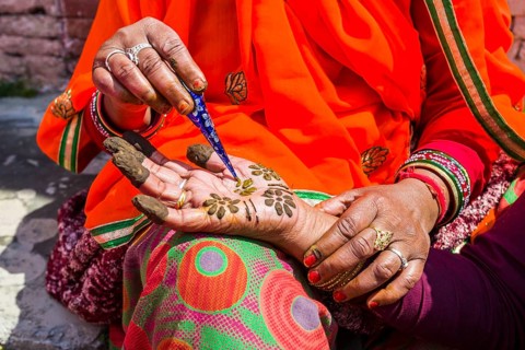An indian woman is painting a hand with henna
