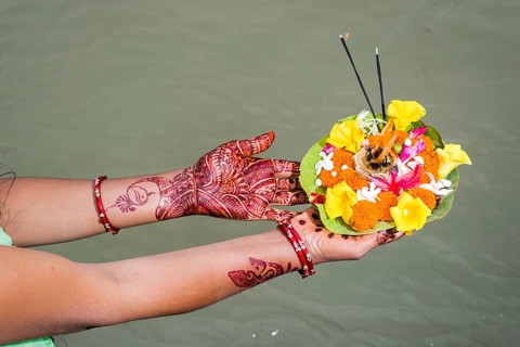 A pair of henna painted hands are holding a deepak
