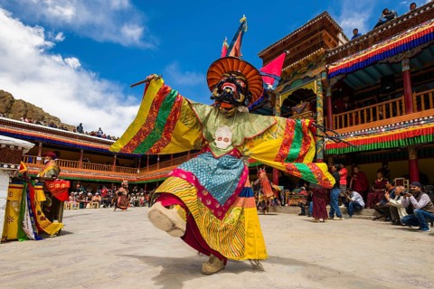 Monks with big wooden masks and colorful costumes are performing ritual dances at Hemis Festival in the courtyard of the monastery