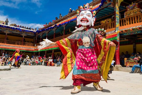 Monks with big wooden masks and colorful costumes are performing ritual dances at Hemis Festival in the courtyard of the monastery