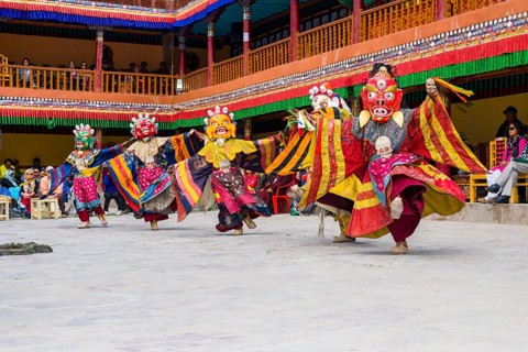 Monks with big wooden masks and colorful costumes are performing ritual dances at Hemis Festival in the courtyard of the monastery