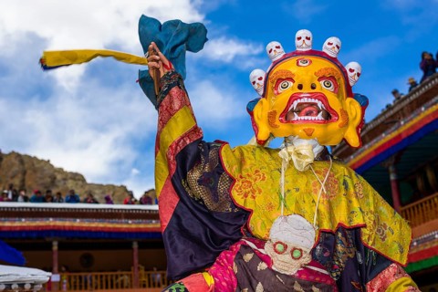 Monks with big wooden masks and colorful costumes are performing ritual dances at Hemis Festival in the courtyard of the monastery