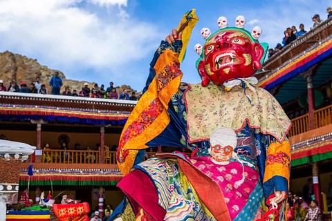 Monks with big wooden masks and colorful costumes are performing ritual dances at Hemis Festival in the courtyard of the monastery