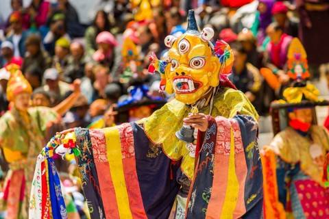 Monks with big wooden masks and colorful costumes are performing ritual dances at Hemis Festival in the courtyard of the monastery