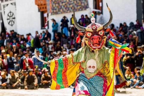 Monks with big wooden masks and colorful costumes are performing ritual dances at Hemis Festival in the courtyard of the monastery
