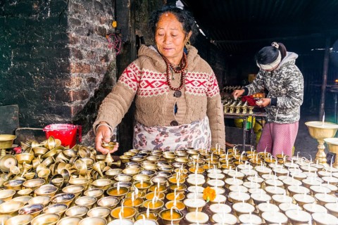 A woman is arranging butter lamps at a temple in Boudha