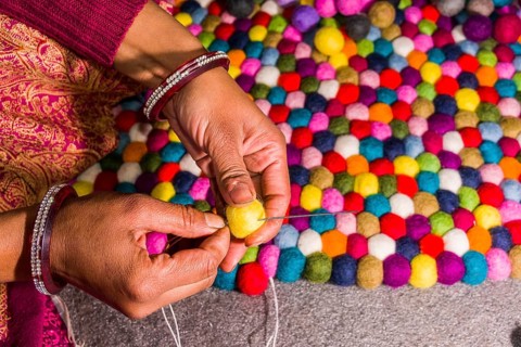 Hands of a woman are producing a carpet from felt balls