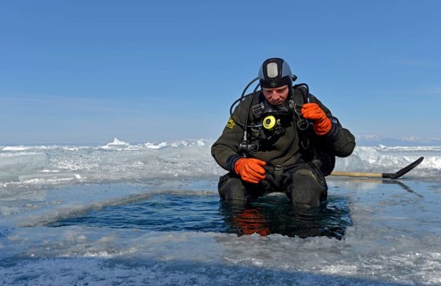 Ice diver by an ice hole preparing to dive