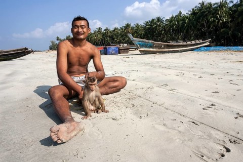 Local man sitting with a monkey on a leash on the beach of the fishing village Ngapali
