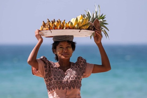 Native woman with a bowl of bananas on her head and Thanaka paste on her face