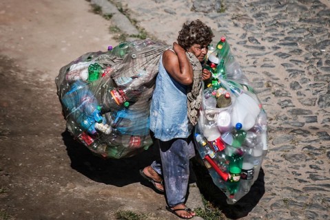 Elderly woman carrying bags with plastic bottles to sell for recycling