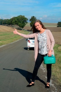 Young brunette woman holding a petrol can hitchhiking on an empty country road