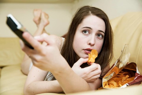 Young woman in underwear watching TV on the sofa with a bag of chips and the remote control in hand
