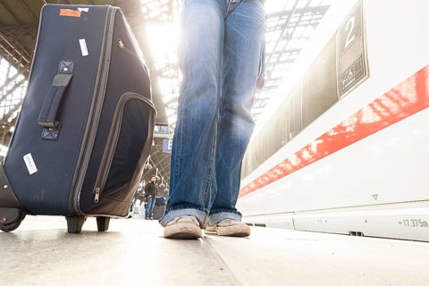 Woman in jeans and sneakers with suitcase waiting at the platform at the train station