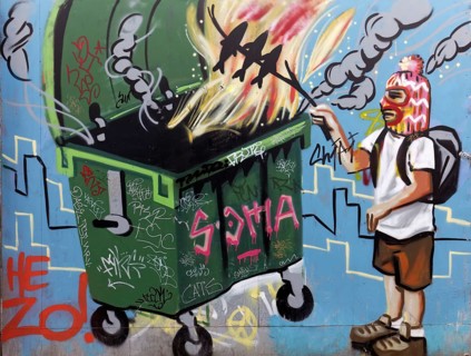 Man with facemask grilling fish over a fire in a dumpster