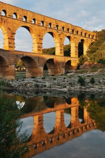 Roman aqueduct Pont du Gard reflected in the Gardon river in the evening